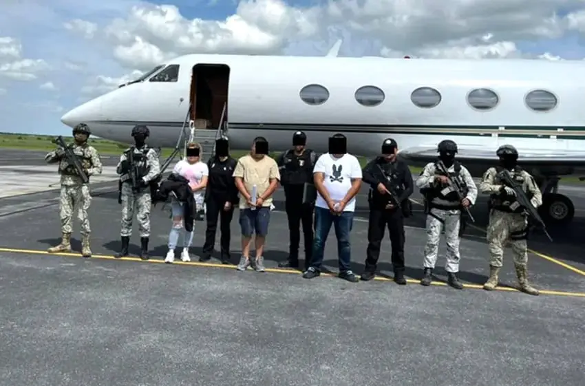 National Guard members stand with three suspects in front of a plane