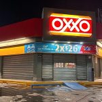 A closed Oxxo store at night with corrugated metal garage style doors covering all doors and windows to the store.