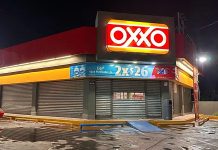 A closed Oxxo store at night with corrugated metal garage style doors covering all doors and windows to the store.