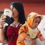 A single mother drinking a beer while holding a baby