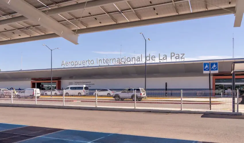 The front entrance to the La Paz, Baja California, international airport, with cars parked in front of the entrance.