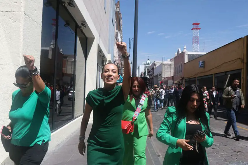 Women in green march through a street in the city of Puebla. At the center foreground is Puebla state Deputy Monica Silva, holding her raised fist in the air,