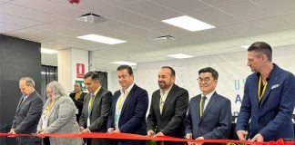 USI officials and officials from Jalisco, Mexico, in a horizontal line all holding part of a red ribbon and holding scissors, readying to cut it as part of an opening ceremony for its new Tonalá plant