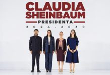 Claudia Sheinbuam stands with her new cabinet appointees on a stage with the words "Claudia Sheinbaum, Presidenta."
