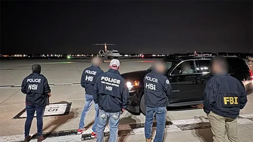 Officials in HSI and FBI jackets stand on an airport tarmac