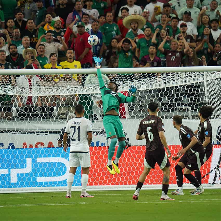 The Ecuadorian goal keeper jumps to push a shot away from the net during a Copa América game, as Mexican fans watch with shocked expressions behind the goal.