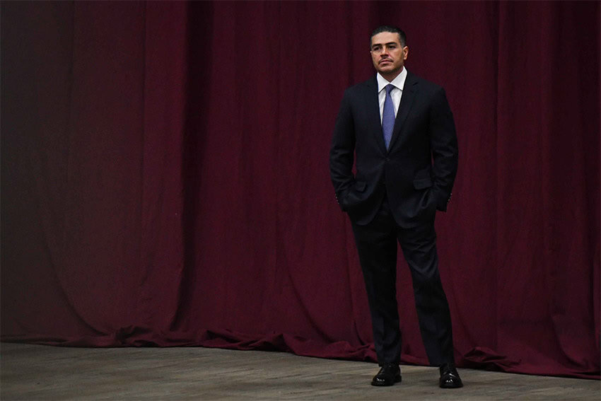 Omar Harfuch, an appointee for Sheinbaum's governing cabinet, stands in front of a red stage curtain wearing a suit
