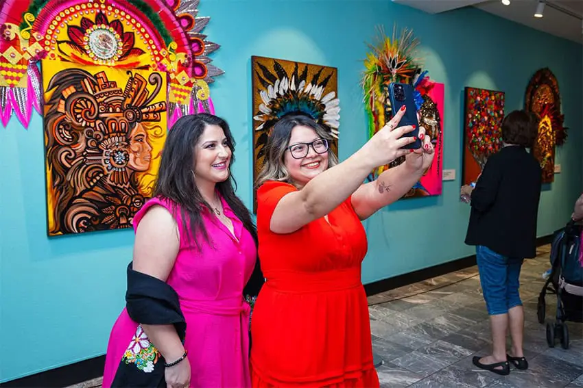 Two women take a selfie in front of colorful multi-media art in a Nashville museumTwo women take a selfie in front of colorful multi-media art with Mexican motifs in a Nashville museum.