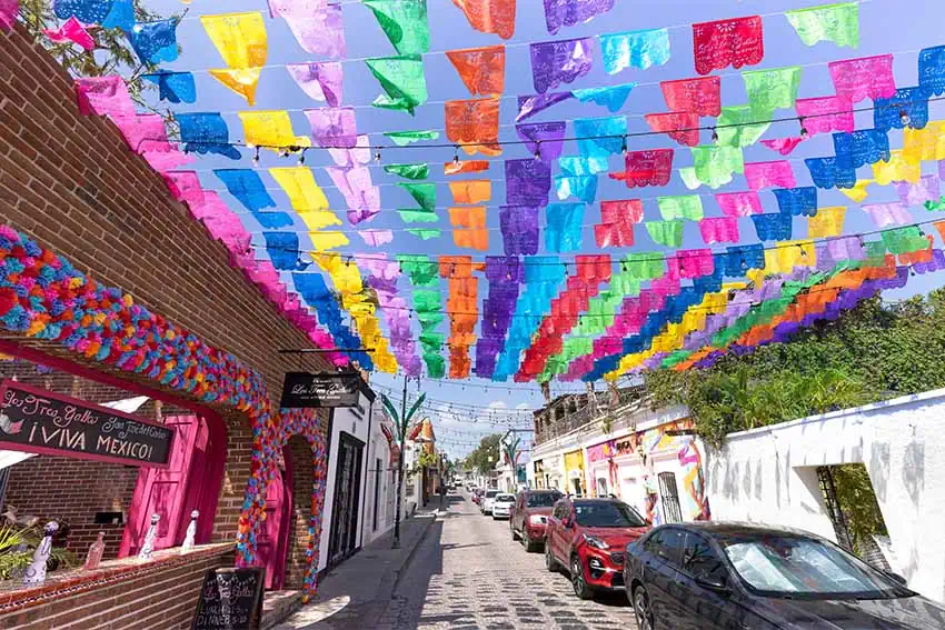 San jose del Cabo, Baja California Sur with papel picada fluttering above a downtown street and cars parked along the sidewalk.