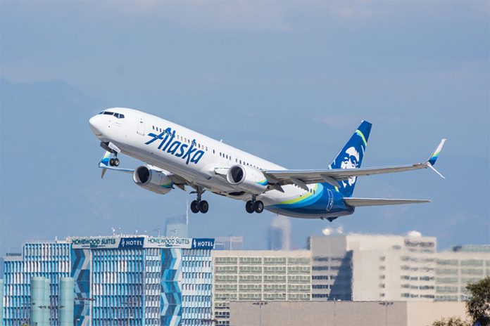 An Alaska Airlines plane taking off over the Los Angeles city skyline