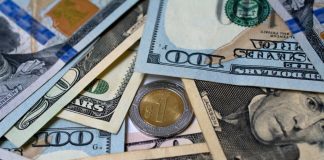 Image of US currency bills of various denominations in a pile around a single Mexican peso coin, which hit a a 4-month high on Friday