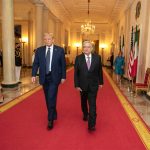 AMLOAMLO and Donald Trump walk down a red carpet in an elegant hallway. and Donald Trump walk down a red carpet in a long corridor.