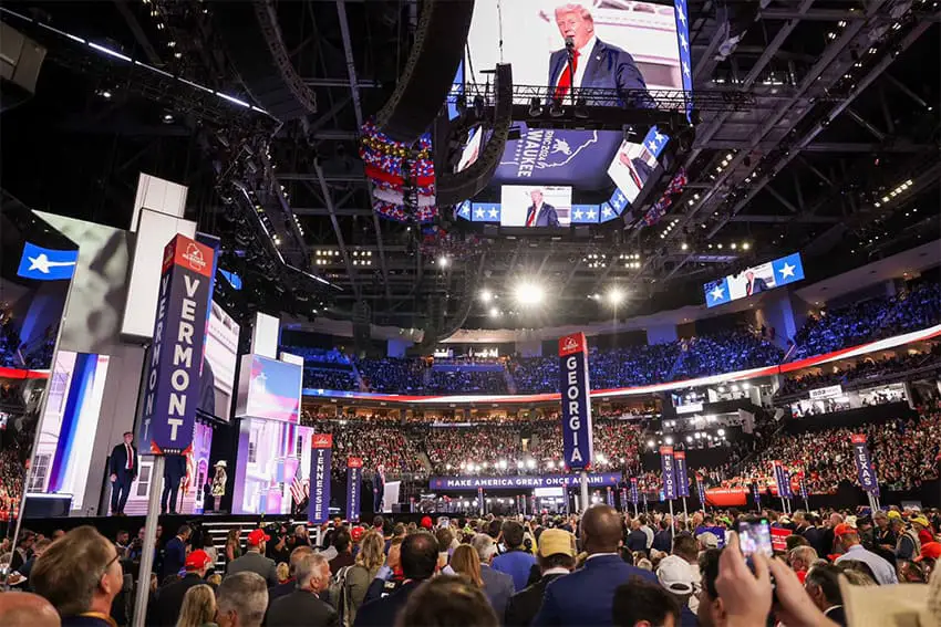 An audience listens to Donald Trump, visible on a overhead screen, as he gives a speech at the Republican National Convention.