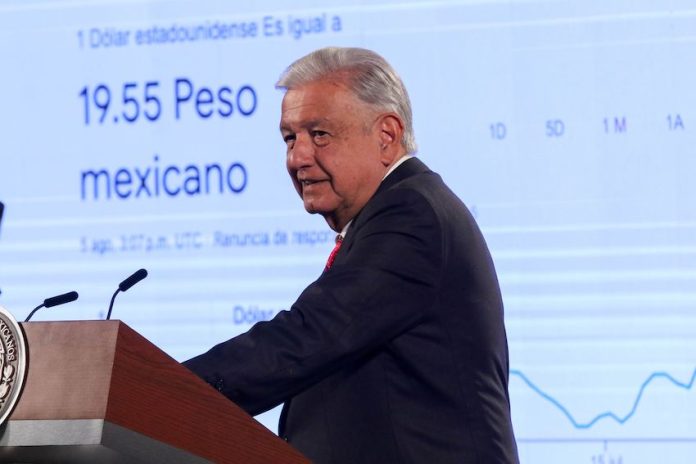 President López Obrador stands in front of a presentation on the dollar-peso exchange rate.