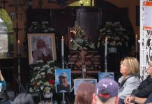 People sitting surrounded by flower arrangements, photos and lit candles at funeral services for murdered journalist Alejandro Martinez