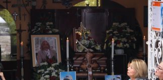 People sitting surrounded by flower arrangements, photos and lit candles at funeral services for murdered journalist Alejandro Martinez