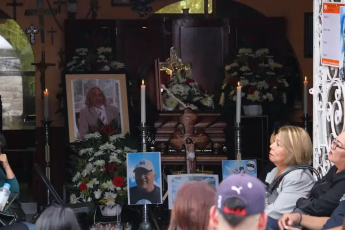 People sitting surrounded by flower arrangements, photos and lit candles at funeral services for murdered journalist Alejandro Martinez