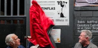 Two older men with a man dressed as Cantinflas pull down a red silk fabric covering a plaque on a building where the iconic Mexican actor grew up.