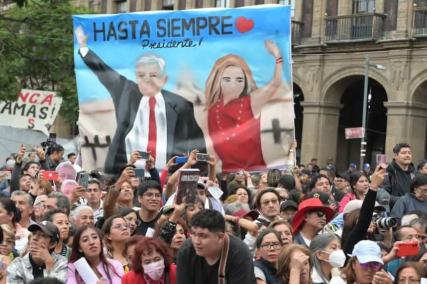 Packed crowds in Mexico City's Zocalo, taking pictures of something onstage with their phones during the presentation of Beatriz Gutierrez Muller's book, "Silent Feminism." Some are holding up a painted banner of President Lopez Obrador and first lady Gutierrez Muller standing next to each other, waving at crowds. The banner says "Hasta Siempre Presidente!"