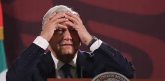 President Lopez Obrador of Mexico standing at a podium at a press conference with his hands on his forehead in a distressed gesture