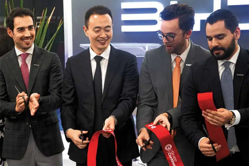 BYD executives in suits holding a thick red ribbon they just cut as part of a showroom-opening ceremony