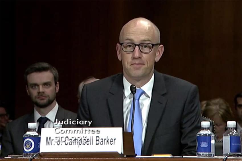 J. Campbell Baker in a suit and blue tie sitting in front of a microphone inside the US Senate