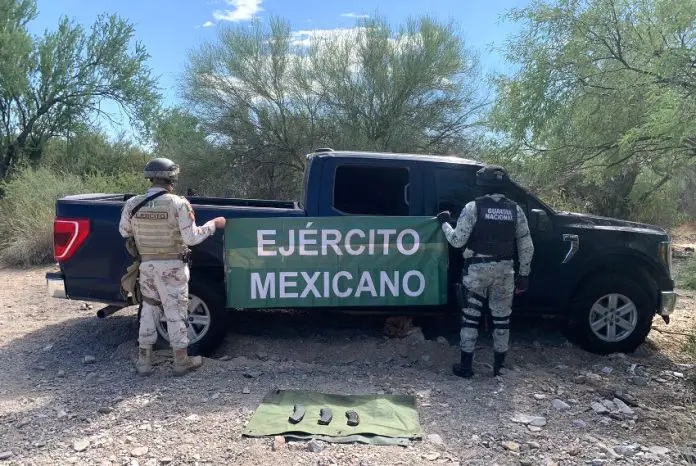 Two soldiers holding up a Mexican army banner by a pickup truck