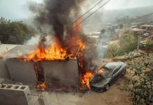 Tesla car in Tijuana next to a gutted building on fire.