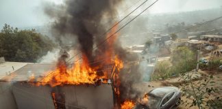 Tesla car in Tijuana next to a gutted building on fire.