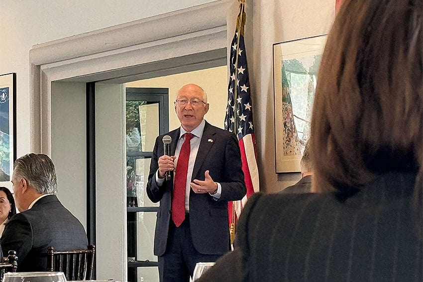 US Ambassador to Mexico Ken Salazar in a suit holding a microphone talking to a room of people.