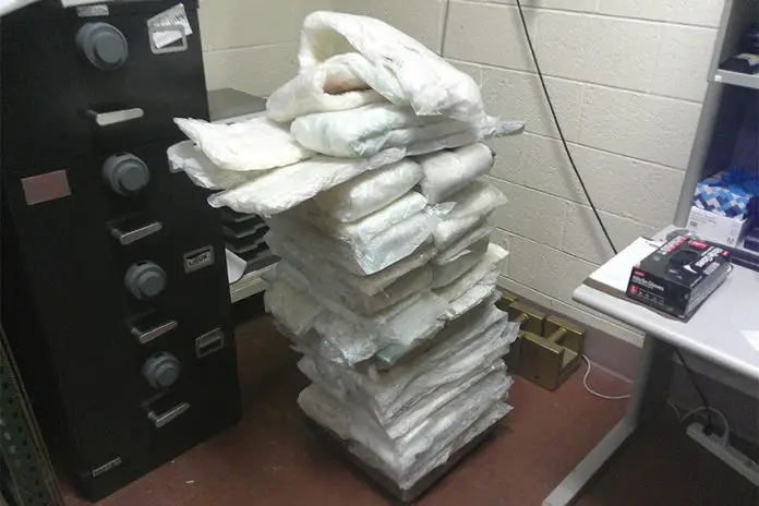 Packages of a white powdery substance suspected to be illicit drugs sitting piled up in a CBP office