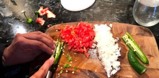 Hands chopping tomato, onion and jalapeño