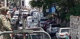 A soldier of the Mexican army standing in the bed of an armored pickup truck behind a traffic jam of other federal and military vehicles blocking a street in Taxco