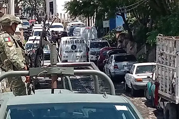 A soldier of the Mexican army standing in the bed of an armored pickup truck behind a traffic jam of other federal and military vehicles blocking a street in Taxco