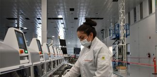 Woman in a white lab coat repairing electronic equipment on an array of computers at the Continental automotive plant in Aguascalientes, Mexico