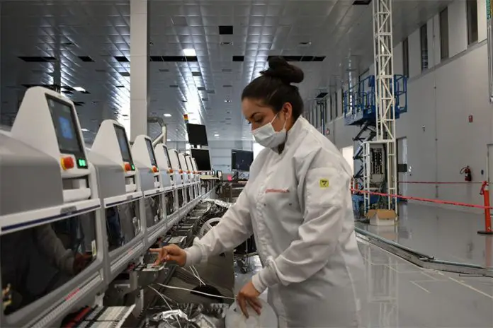 Woman in a white lab coat repairing electronic equipment on an array of computers at the Continental automotive plant in Aguascalientes, Mexico