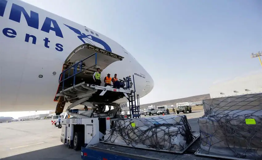 Cargo handlers standing on an open plane in front of large cargo on the ground below them.