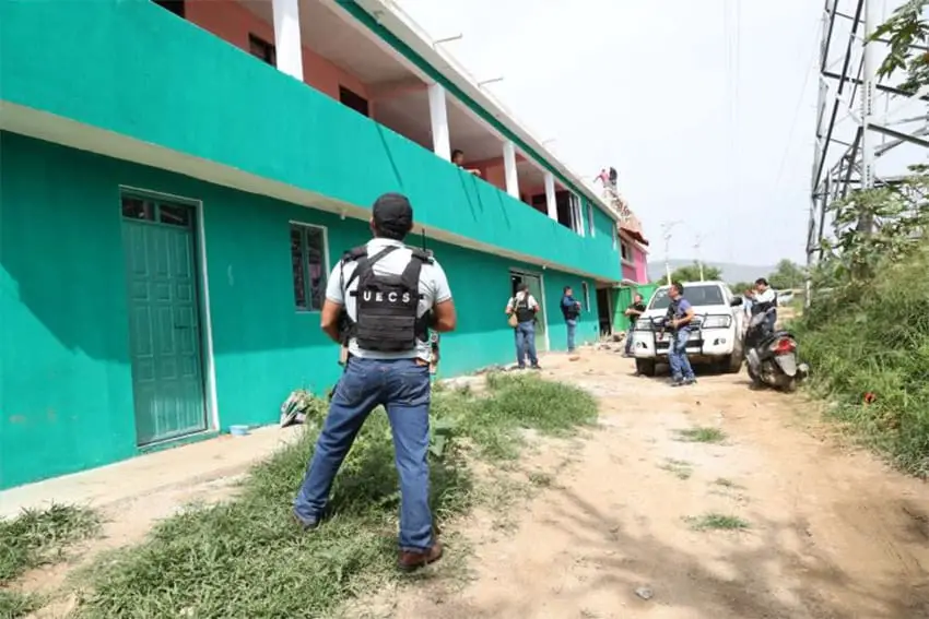 La policía se encuentra afuera de un edificio verde frente a un lote abandonado, donde los migrantes fueron rescatados en Oaxaca.