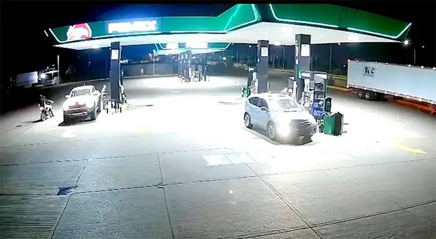 Men on a motorcycle next to a white SUV in a gas station at night.