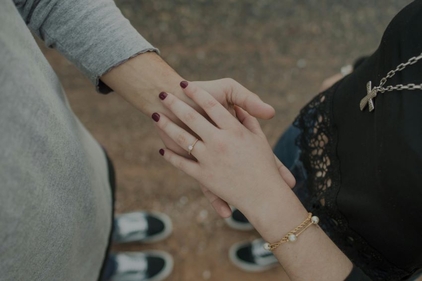 Bird's eye view of woman's hand with wedding ring resting on top of man's hand.