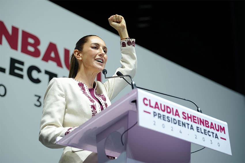 La presidenta electa Claudia Sheinbaum levanta el puño mientras habla en un podio.