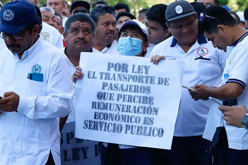 Mexican male taxi drivers standing outside at a protest. Two of them are holding a sign in Spanish saying that taxi service is a public service