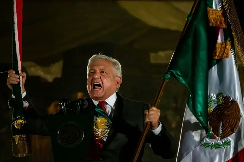 Mexico's President Lopez Obrador dressed in a suit and a ceremonial sash in the colors of the Mexican flag, shouting while he holds a flag of Mexico and a ceremonial staff