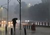 Resident of Mexico City walking with an umbrella near a highway in heavy rains and fog.