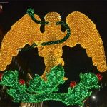 Light mosaic of a yellow eagle with a green serpent in its beak standing on a cactus tree, surrounded nearby by historic buildings in Mexico City's main square