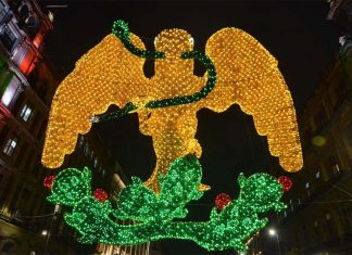 Light mosaic of a yellow eagle with a green serpent in its beak standing on a cactus tree, surrounded nearby by historic buildings in Mexico City's main square