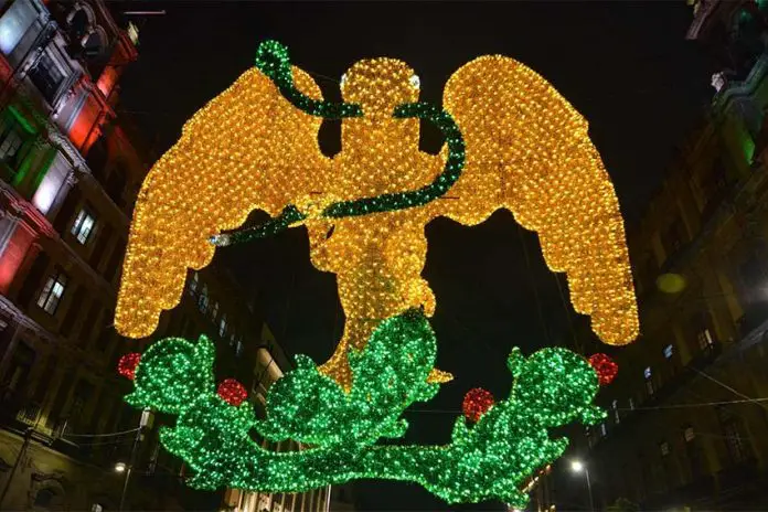 Light mosaic of a yellow eagle with a green serpent in its beak standing on a cactus tree, surrounded nearby by historic buildings in Mexico City's main square