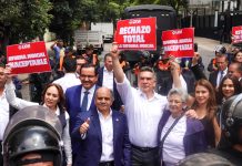 Mexican senators in suits hold signs reading "rechazo total" while standing in front of judicial reform protesters in the streets of Mexico City