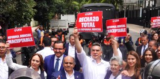 Mexican senators in suits hold signs reading "rechazo total" while standing in front of judicial reform protesters in the streets of Mexico City