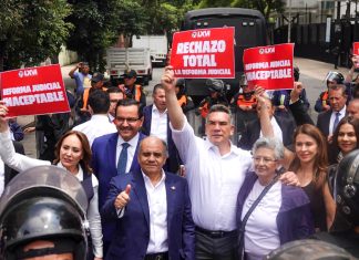 Mexican senators in suits hold signs reading "rechazo total" while standing in front of judicial reform protesters in the streets of Mexico City